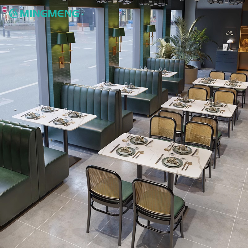 Stylish canteen-style dining area arranged with black rattan back chairs, green leather seats, and sleek white marble tables under natural daylight