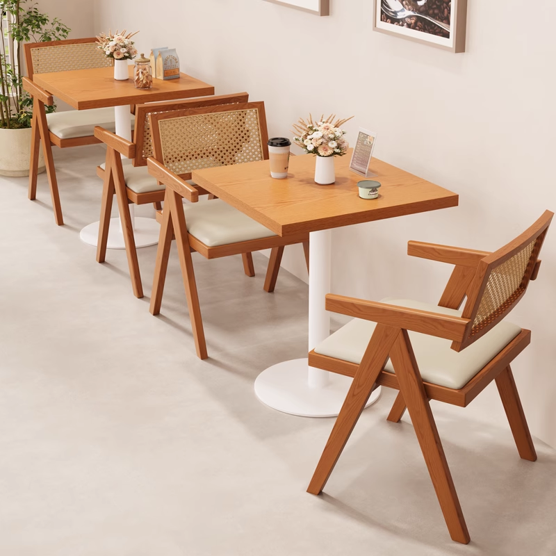 Rattan-back wooden dining chairs with white cushions placed around square café tables in a warm, modern interior