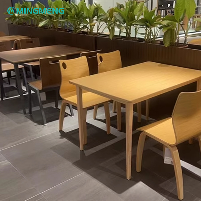 Modern cafeteria setup with multiple square wood dining tables and matching curved-back wooden chairs in a plant-lined space