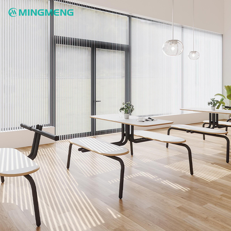 Minimalist white canteen dining benches with black handles placed beside tall windows, highlighted by soft natural light and indoor greenery
