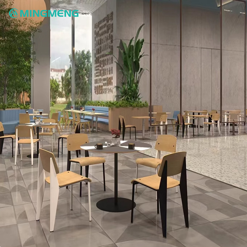 Multiple wooden canteen chairs with black and white legs paired with round tables in a modern dining hall