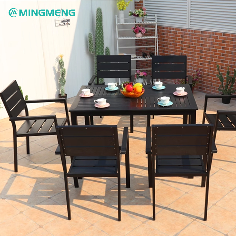 Black plastic wood dining table with seven matching outdoor chairs in a cozy patio setting