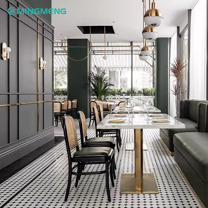 Upscale dining interior featuring classic rattan back dining chairs paired with marble-top tables, designer lighting, and green leather booth seating
