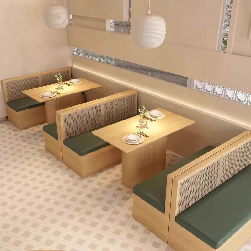 Cozy restaurant setting featuring light wood booth seating with rattan backrests and dark green cushions arranged in pairs