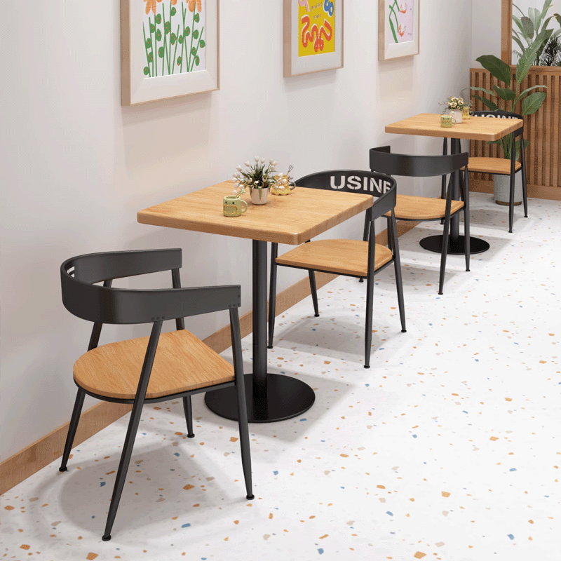 Square wood dining table with minimalist black base and wooden chairs in cafe setting