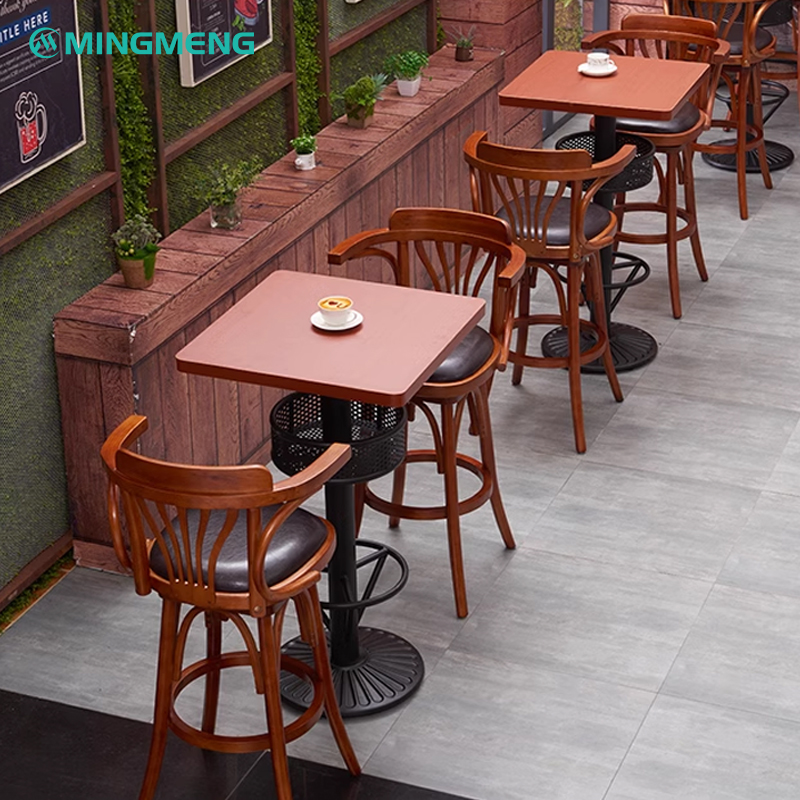 Nordic bar table with two wooden stools and black round base in a cafe setting with plants and wall art.