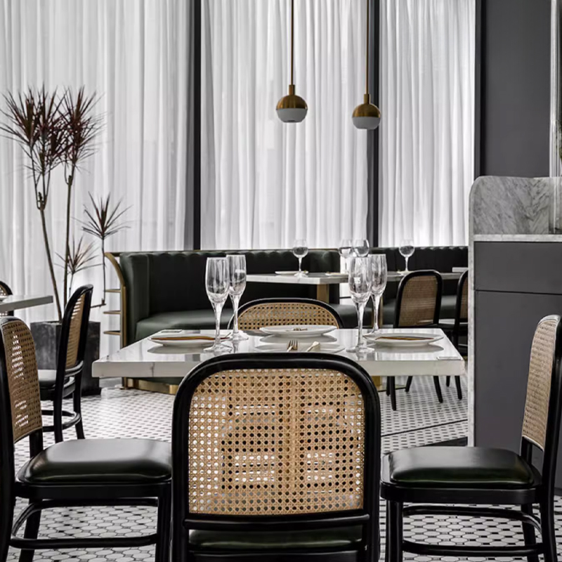 Vintage Rattan Back Restaurant Chair Upscale dining interior featuring classic rattan back dining chairs paired with marble-top tables, designer lighting, and green leather booth seating