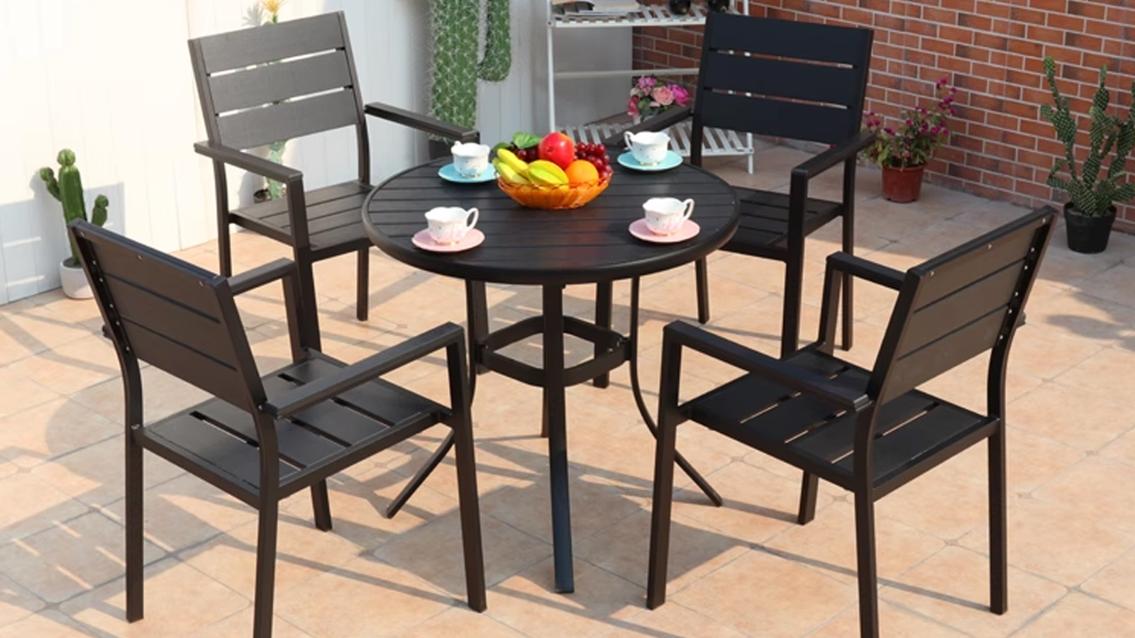Black Plastic Wood Outdoor Armchair Round outdoor dining table with black plastic wood chairs and fruit bowl centerpiece on a patio