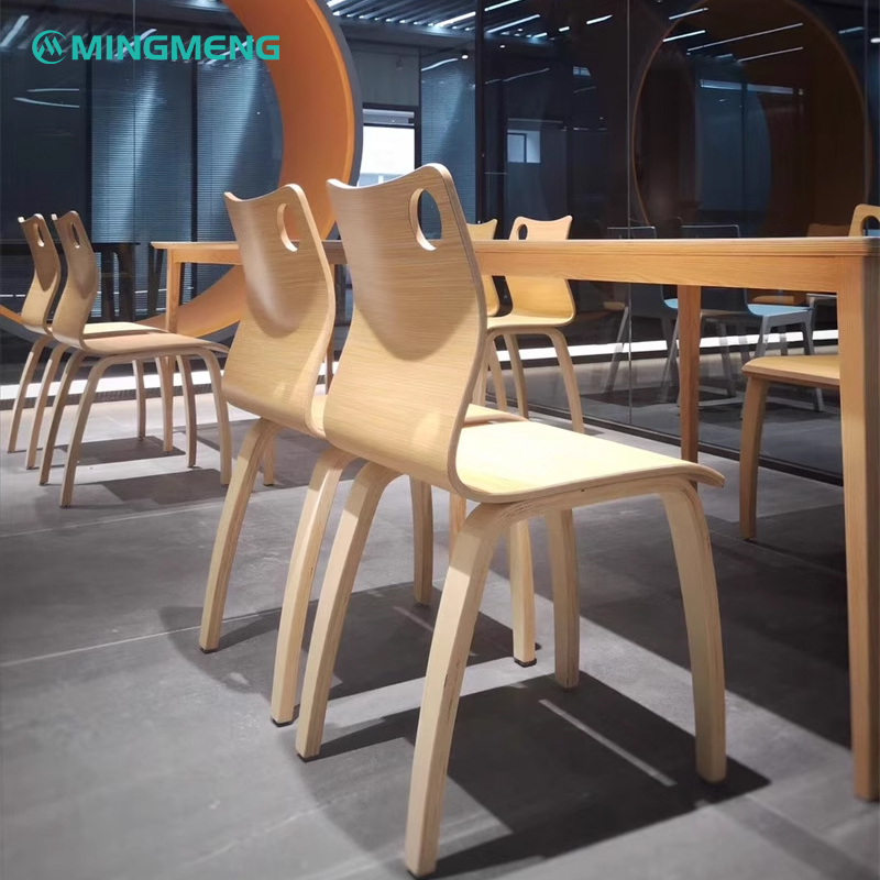 Multiple light wood dining chairs with curved backs arranged along a long rectangular table in a canteen or meeting room