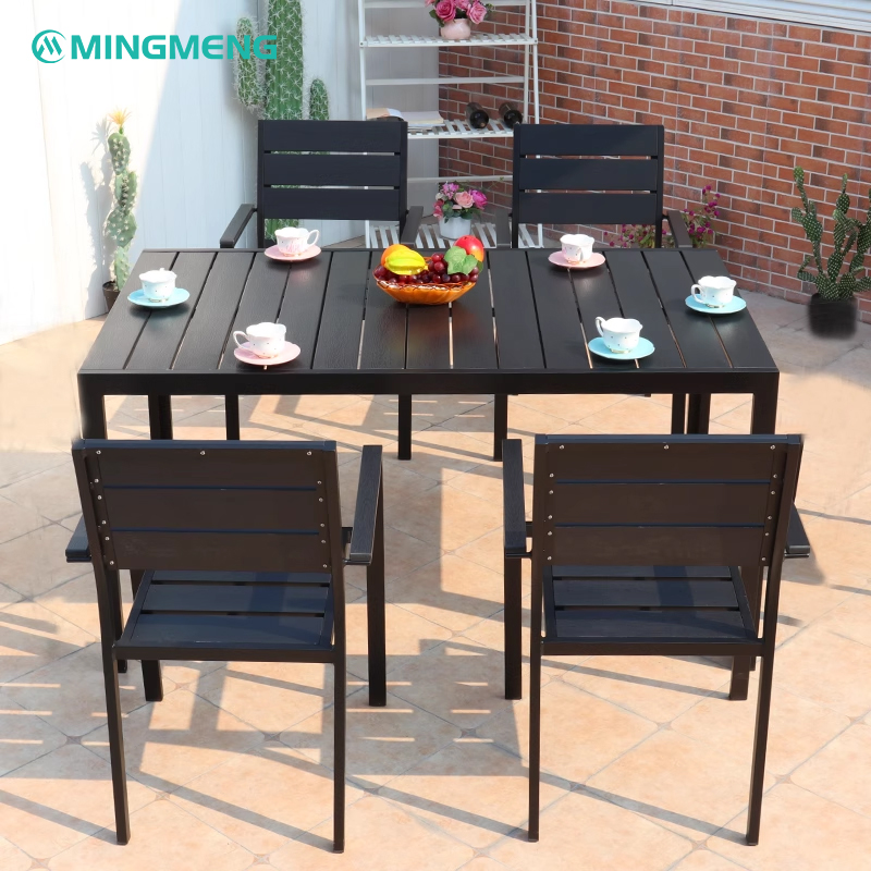 Terrace dining setup featuring a long black table with six plastic wood chairs and a colorful fruit bowl centerpiece