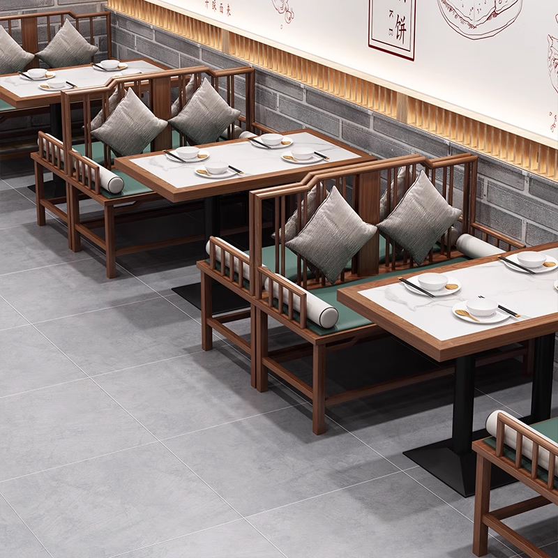 A cozy dining area featuring wooden booth seating with green cushions, decorative pillows, and elegant tables with white ceramic plates