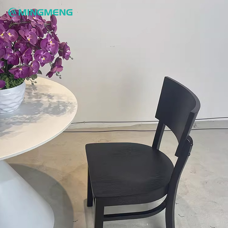 Black wood restaurant chair with a solid backrest, shown next to a white round dining table with purple flowers