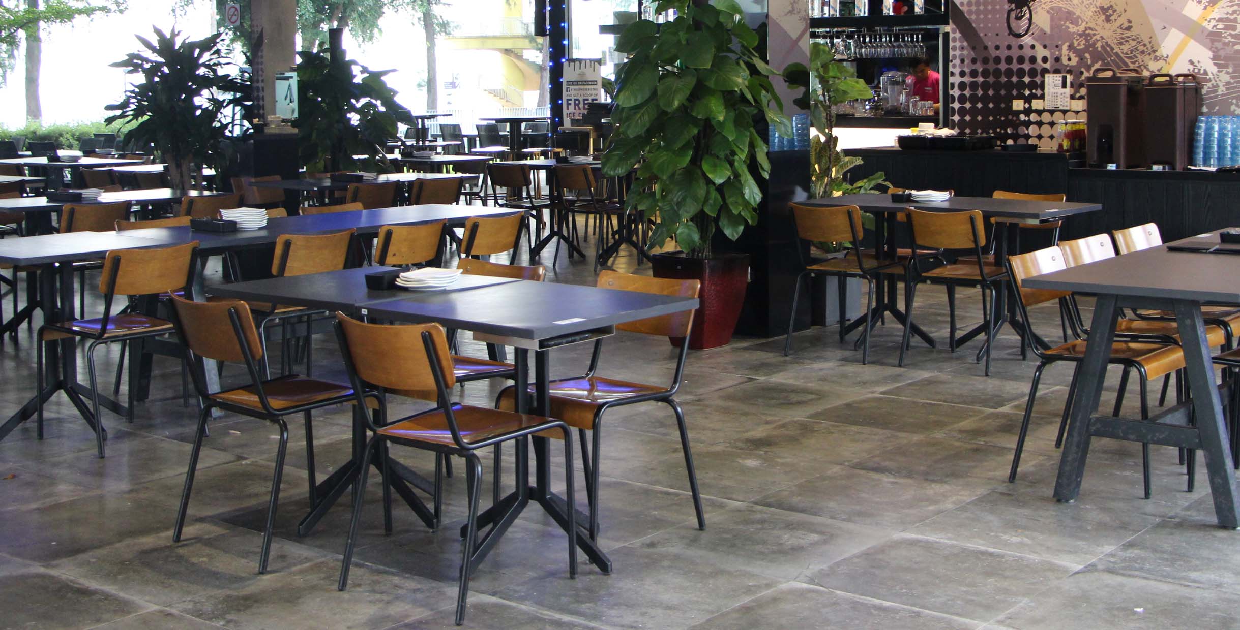 Modern café furniture setup with black dining tables and wooden chairs in a spacious coffee shop interior.