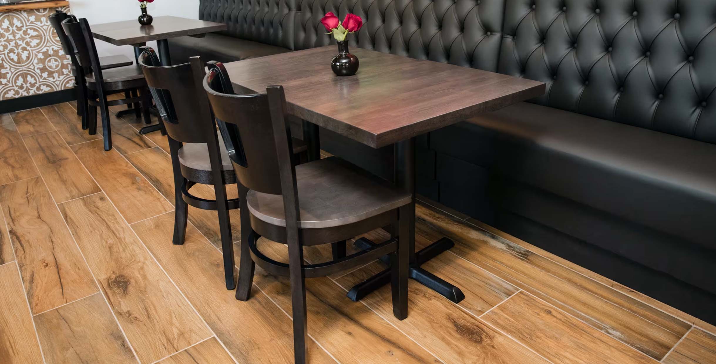 Restaurant dining setup with dark wood chairs, square wooden tables, and black tufted booth seating