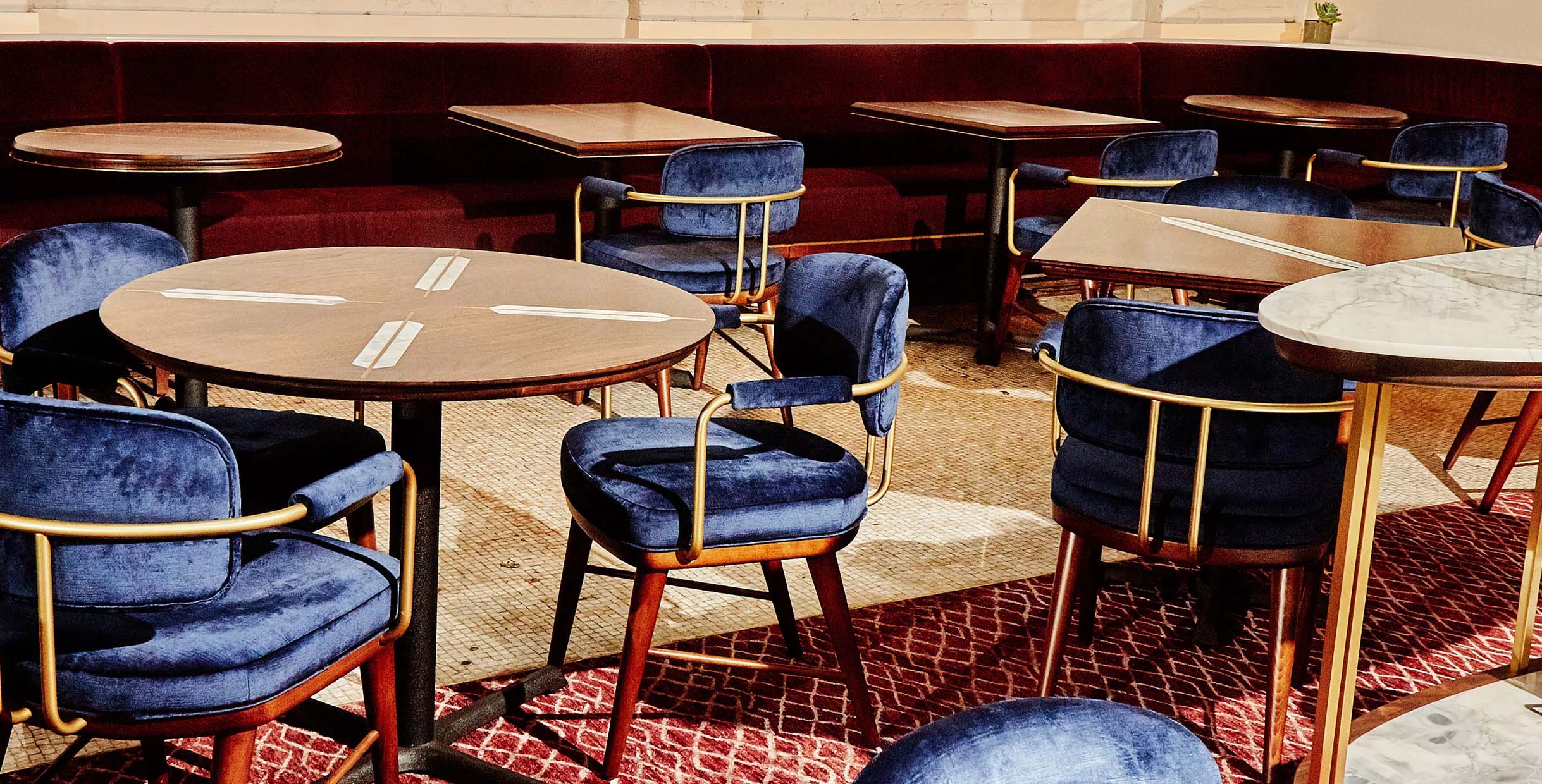 Elegant restaurant booth sofa with deep red upholstery paired with blue velvet chairs and wooden dining tables.