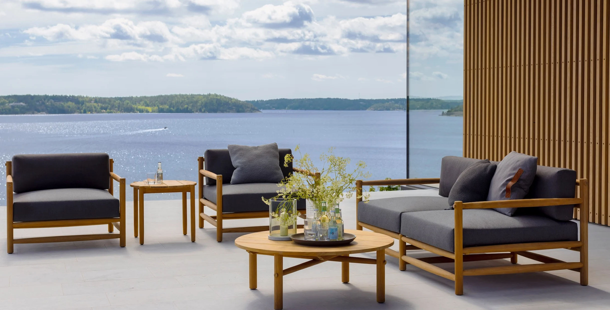 Contemporary outdoor furniture set with wooden frame and grey cushions overlooking the sea