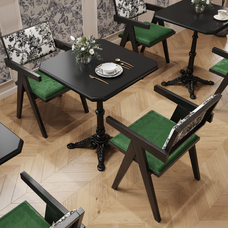Contemporary restaurant chair with green cushion and black floral patterned backrest around square dining tables.
