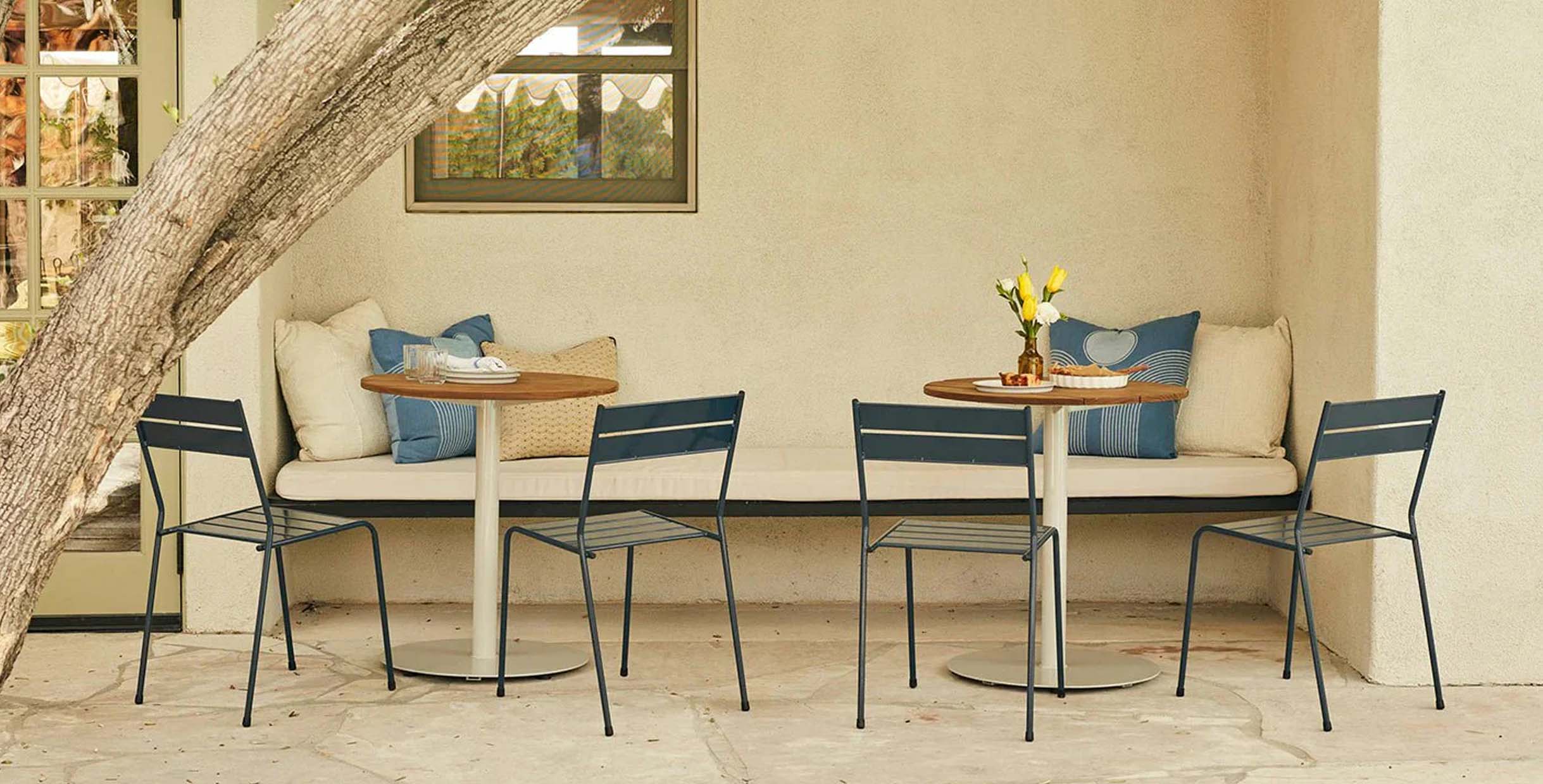 Outdoor café furniture with metal chairs and round wooden tables next to a cozy cushioned patio bench.