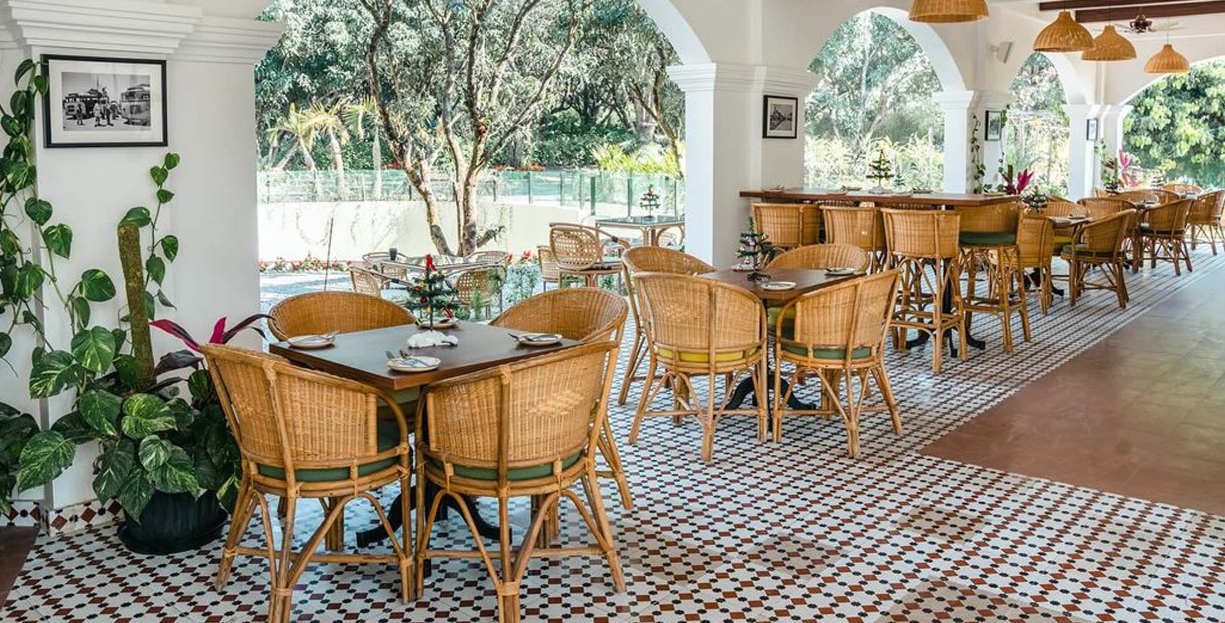 Outdoor café furniture with rattan chairs and wooden tables in a bright garden restaurant setting.