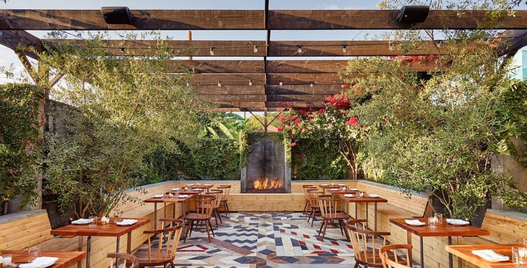 California style dining area with stylish tables and chairs at a restaurant, featuring a cozy atmosphere with plants and a fire pit