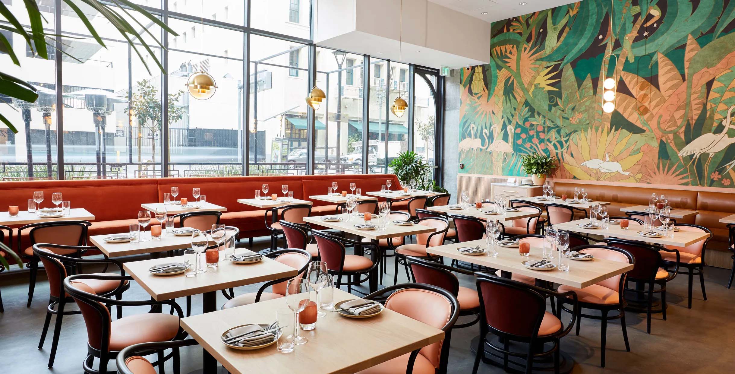 Modern restaurant booth sofas with orange upholstery, black dining chairs, and artistic mural wall decor in a bright dining space.
