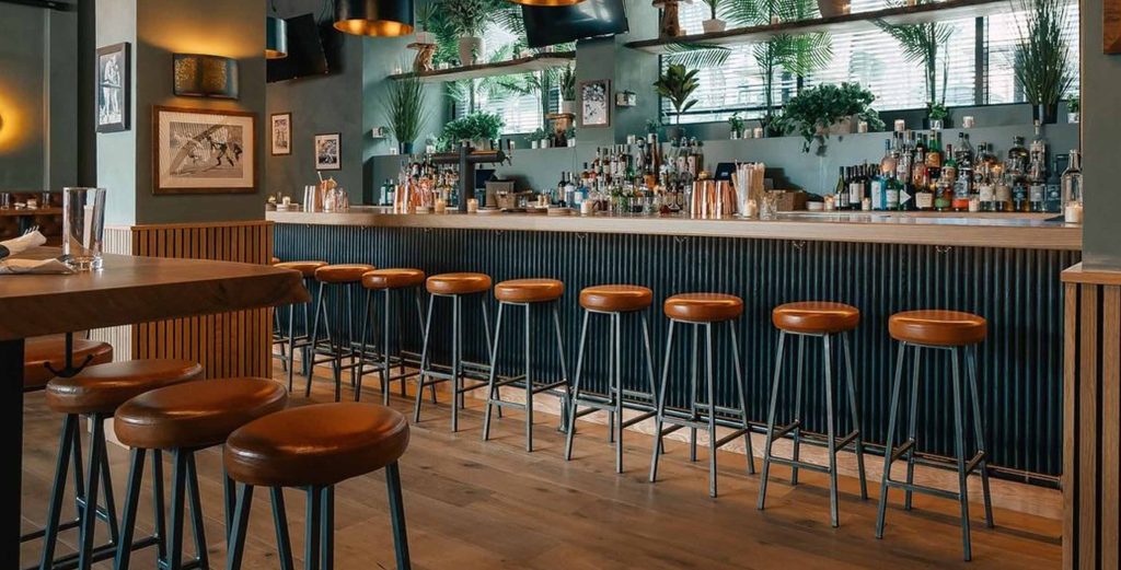 Commercial-grade wooden bar stools with leather cushions arranged along a modern café bar counter.