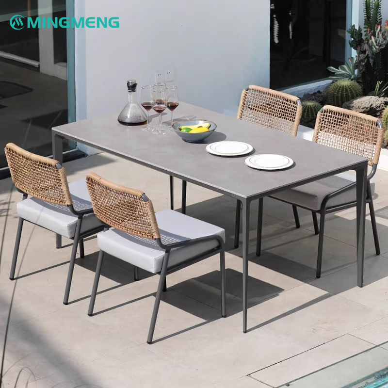 Custom Nordic Outdoor Rattan Dining Chair2 Outdoor dining table set with four woven chairs, placed on a modern patio with plates and wine glasses on the table.