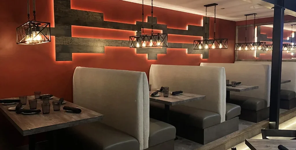 Top 10 Custom Restaurant Booth Manufacturers in the USA (2025 Guide)1 Custom high-back restaurant booth seating with neutral upholstery and wood tables in an industrial-style dining space