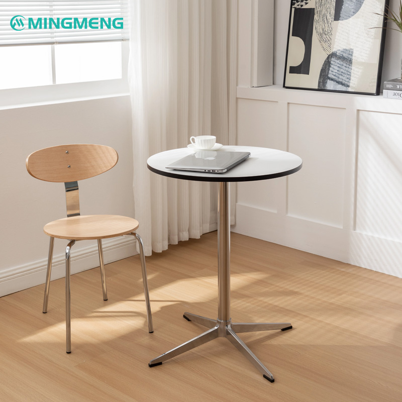 Modern stainless steel café table with white round top and wooden chair in bright minimalist interior